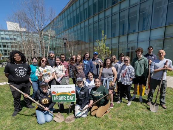 Arbor Day 2024. A group of students congregate around a white sign which says "Arbor Day" in front of the Nettie Science Building on campus. Professor Tim Parshall is with them. Two students in the front hold shovels.