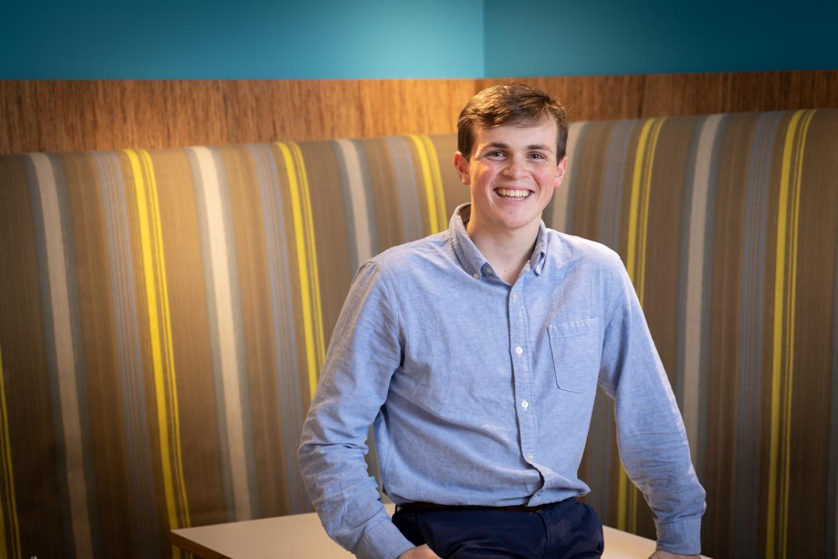 Student smiling sitting at a table with a striped background.