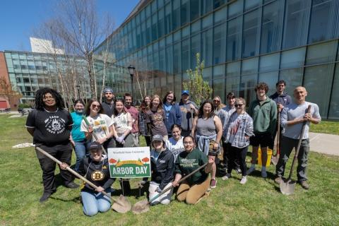 Arbor Day 2024. A group of students congregate around a white sign which says "Arbor Day" in front of the Nettie Science Building on campus. Professor Tim Parshall is with them. Two students in the front hold shovels.