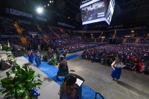 Commencement 2024. Students, faculty, and families are packed in the MassMutual Center in Springfield, with a screen overhead to show students getting their diplomas.