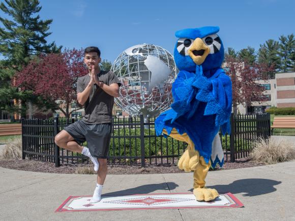 Nestor the Owl and student doing a yoga pose in front of the Globe on the campus green