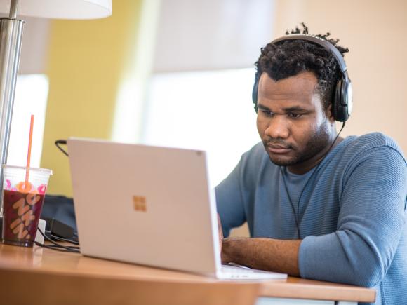 male student, wearing headphones, working on laptop computer in the Ely Library