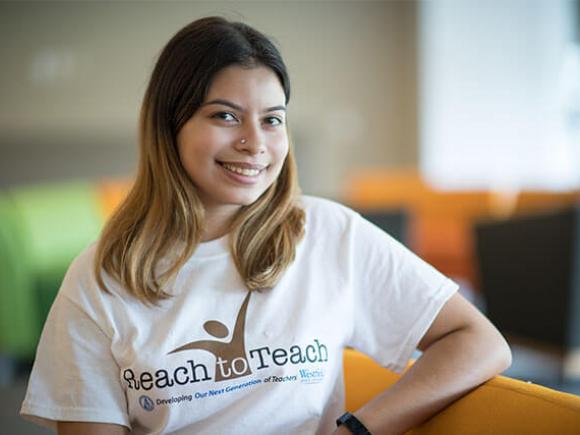 A Westfield University student wearing a “Reach to Teach” T-shirt smiles while posing for a photo.