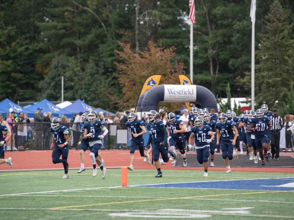 The Owl football team, dressed in blue jerseys, run across the field as they prepare to play.