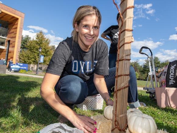 During the scarecrow contest -- a faculty member smiles at the camera while she decorates a wooden stake.