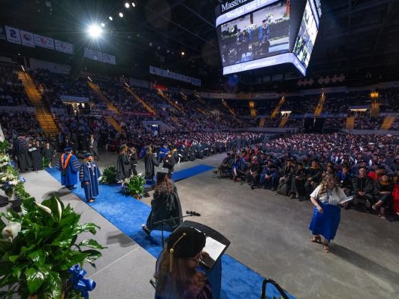 Commencement 2024. Students, faculty, and families are packed in the MassMutual Center in Springfield, with a screen overhead to show students getting their diplomas.