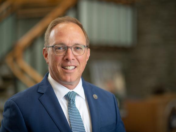 A headshot of Dr. Kevin Hearn, Vice President of Enrollment Management and Student Affairs at Westfield State. He is standing in the Horace Mann lobby, with the background behind him blurred out.