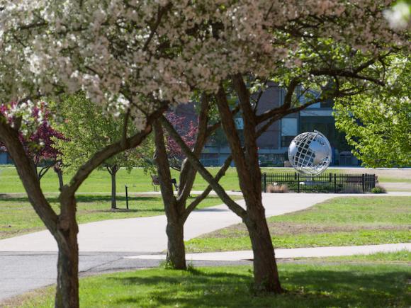 A stock photo of the campus globe. Several flowered threes border the walkway to the globe.
