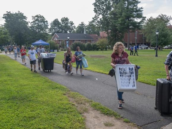 New students and families moving in during the campus' annual Move-In Day. Several people are carrying laundry baskets and other various items as they prepare for the new semester.