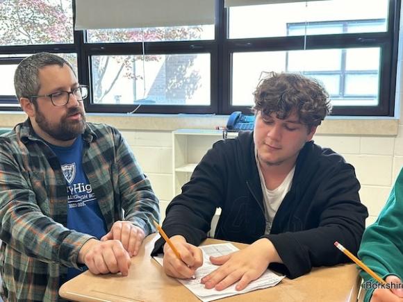 Westfield State alum and math teacher at Drury High School, Mark Brown. He is in a flannel and blue shirt as he helps one of his students in the classroom with the math lesson.