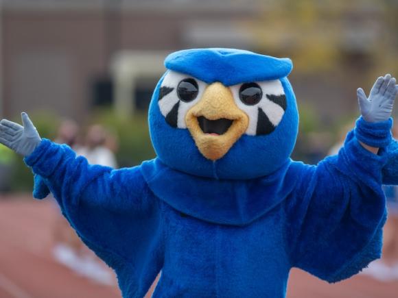 A photo of Nestor the Owl with his hands raised in celebration for the 2024 Family Weekend event! 