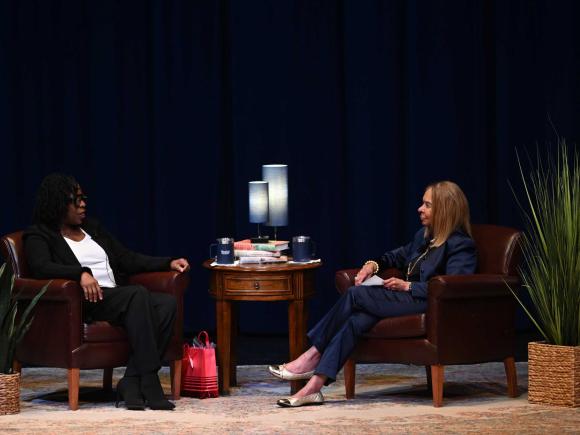 two women sit on a stage in conversation