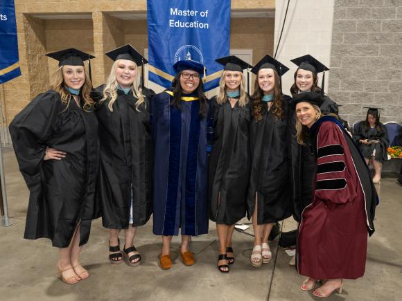 Master of Education students smiling with faculty during commencement ceremony.