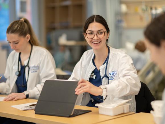 Smiling nursing student opening a laptop in a classroom.