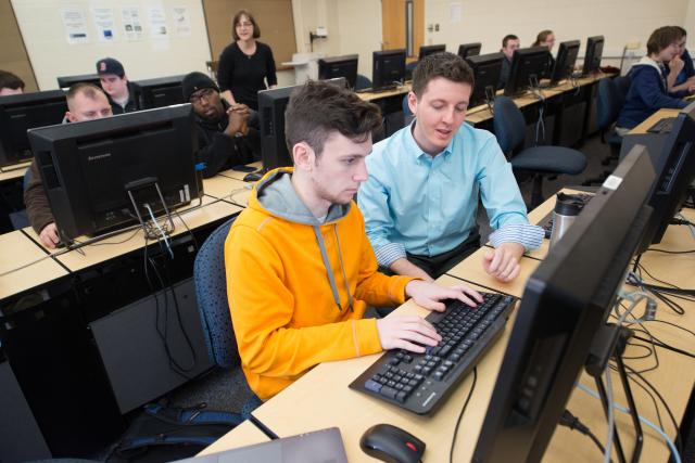 Student at workstation in computer lab as their professor assists