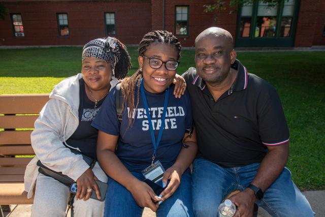 Female student flanked by her parents on move-in day in front of Courtney Hall