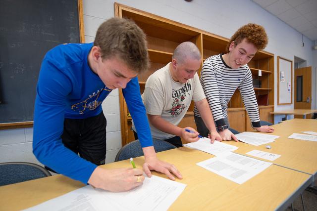 Three students work together on coursework in a history classroom.
