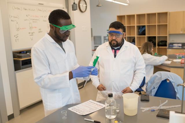 Chemistry student and professor in white lab coats working together in classroom.