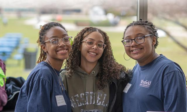 3 female students, in Westfield State shirts, smile towards the camera