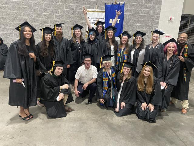 Graphic design students wearing caps and gowns in commencement group photo.