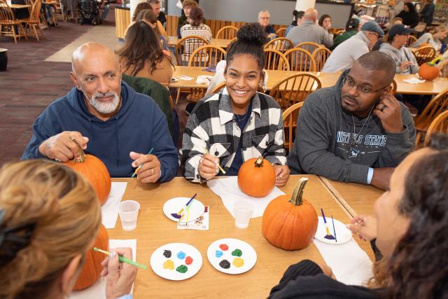 A family smiling painting pumpkins at Family Weekend.