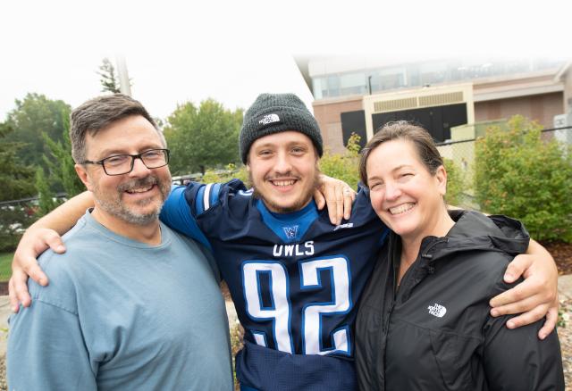 Westfield State football player, flanked by his parents, smiles at the camera during Family Day