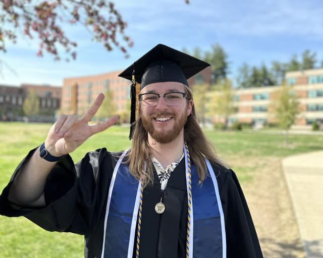 Student in cap and gown holding up two fingers to represent two days until commencement.