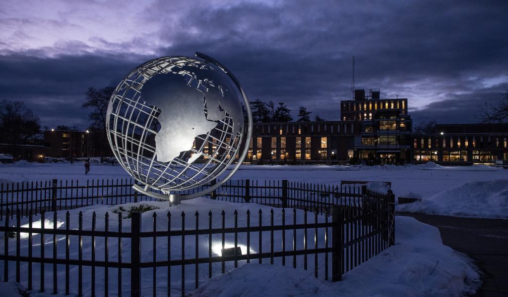 Campus globe at night lit up with snow surrounding it and dark clouds in the sky.