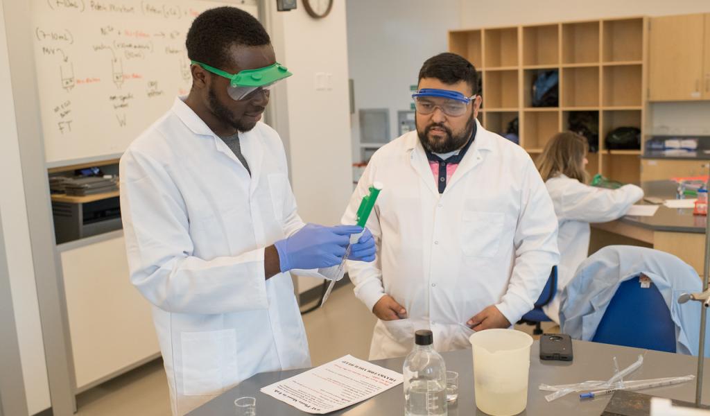 Chemistry student and professor in white lab coats working together in classroom.