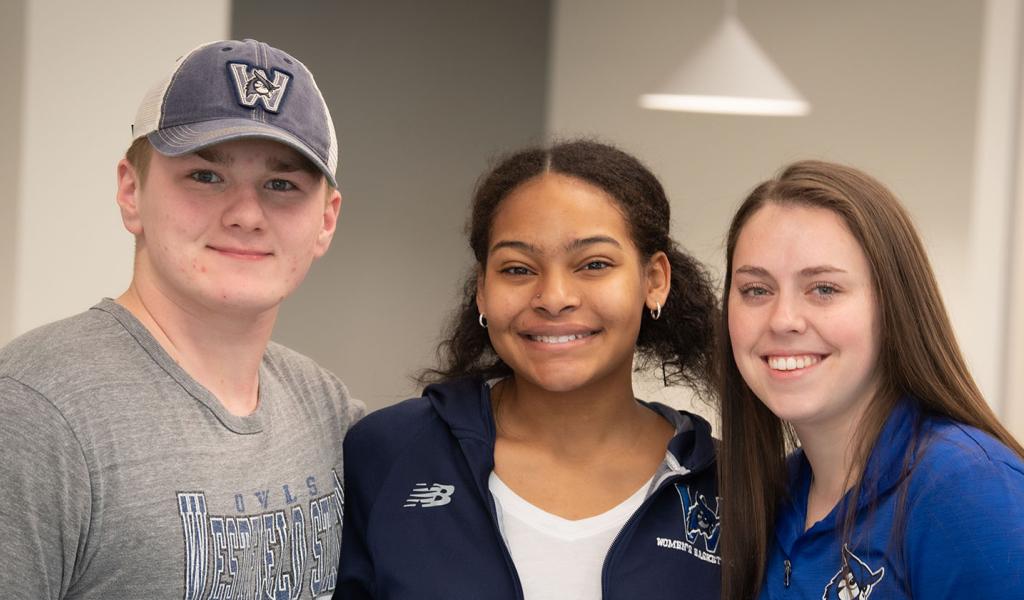 Three Westfield State University students stand together and smile for a photo.