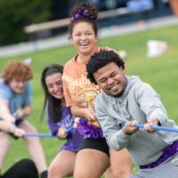 Five students play tug of war with a blue rope