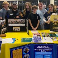 Group of students stand behind the Campus Activities Board table with display posters and handouts 